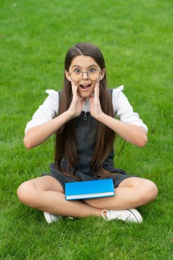 Shocked teen school girl sitting legs crossed on grass. School and education. Back to school.