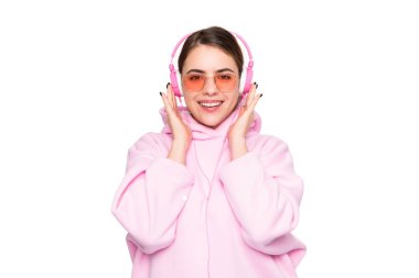 Happy young woman student in casual pink hoodie and glasses listening to online audio course in headphones isolated on white.