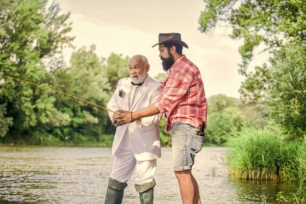 Bearded man and elegant businessman fish together. Learn to fish. Fishing skills. Fish with companion who can offer help in emergency. Men friends relaxing nature background. Personal instructor.