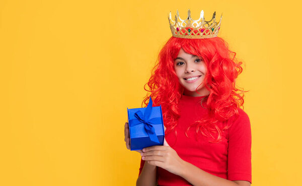 улыбающийся ребенок в диадеме с настоящей коробкой на желтом фоне.