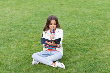 thinking teen child making notes in notebook sitting on grass. taking notes. student make notes outdoor.