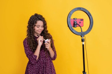 cheerful child blogger with long curly hair making video for blog hold powder brush.