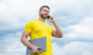 man with computer talking on smartphone on sky background.
