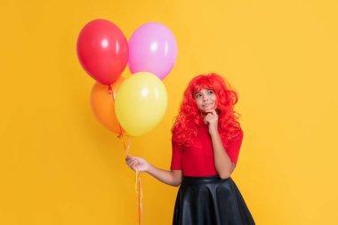 pondering teen girl with party balloon on yellow background.