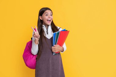 shocked child with school backpack and workbook on yellow background.