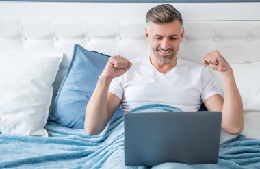 happy mature man working on laptop in bed.
