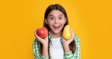 amazed kid with fresh apple and pear on yellow background.