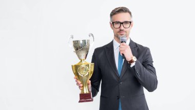 positive mature man in suit hold champion cup and microphone isolated on white background.