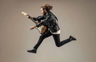 duygusal sakallı rock müzisyeni deri ceketle elektro gitar çalıyor ve zıplıyor, müzik çalıyor..