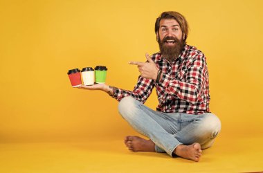 Kareli gömlekli, modaya uygun saç stili olan beyaz, olgun bir hippi sabah kahvesini kağıt bardaktan, sıcak içecekten seçer..