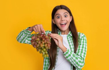 amazed teen girl with grapes fruit on yellow background.