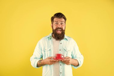 Sarı arka planda sakallı neşeli hippi kahve fincanı tutuyor, sabah.