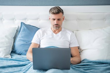 concentrated mature man working on laptop in bed.