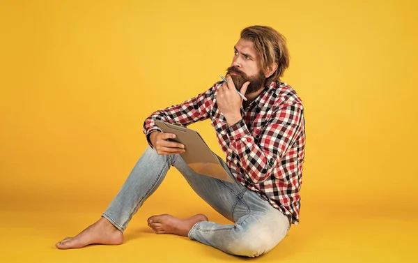 thoughtful handsome bearded guy with unshaven face and stylish hairdo wear casual clothes writing in paper, making notes.