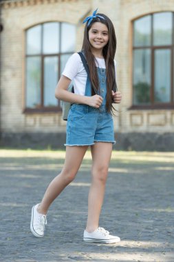 cheerful denim girl with backpack walking outdoor.
