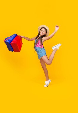 happy teen kid hurry with shopping bags on yellow background. full length.