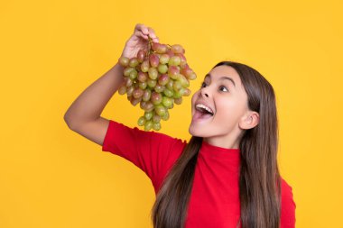 amazed child eat bunch of grapes on yellow background.