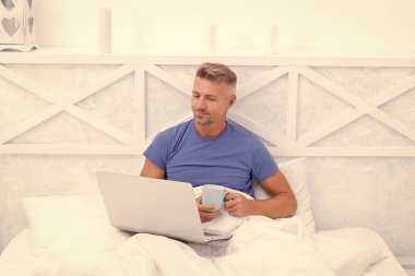 Yatakta dinleniyor. Mutlu adam laptop kullanarak çay içer. Rahatlama zamanı. Sabah rahatlaması. Çevrimiçi sohbet. İnternet sörfünün tadını çıkarıyorum.