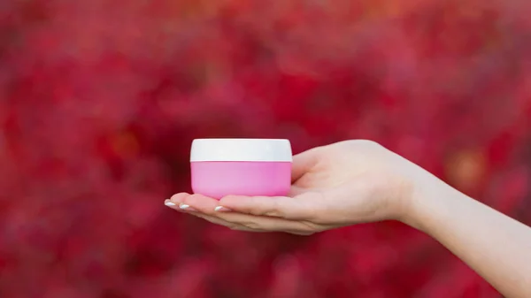 hands holding cream or lotion jar for skincare.