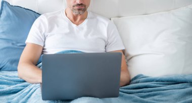 mature man working on laptop in bed. business online.