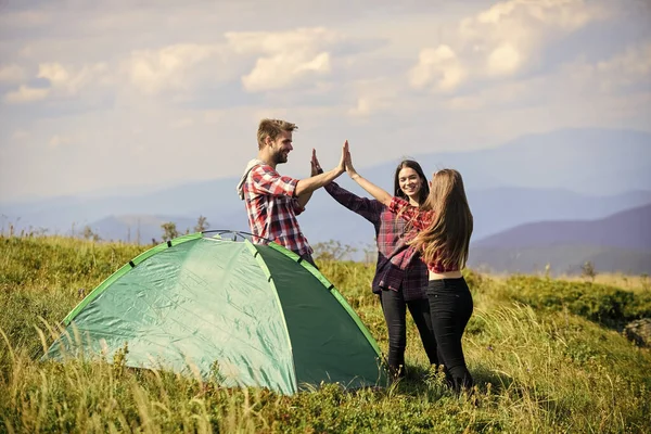 Well done. Camping gear. Camping tent. Good job. Teamwork concept. Hiking activity. Friends set up tent on top mountain. Camping equipment. Weekend in mountains. Man and girls having fun in nature.