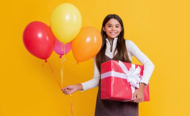 positive child with party colorful balloons and present box on yellow background.