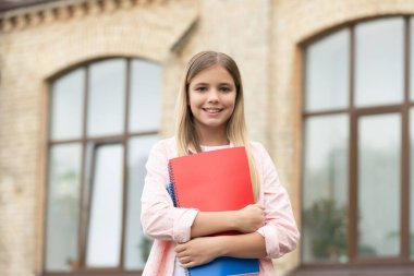 Happy teen girl back-to-school on September 1 holding books outdoors, education.