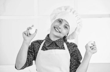 Özel yemek yapıyorum. Yumurta tutan mutlu genç kız. Çocuk pastanede şef üniforması giyiyor. Şapkalı ve önlüklü çocuk. Aşçı mutfakta yumurta hazırla. Sağlıklı yararlı yiyecekler. Mutlu çocukluk. sağlıklı malzemeler.