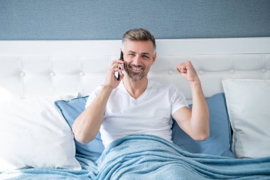 successful mature man in bed speaking on phone.
