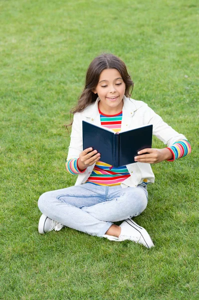 inspired teen girl read book sitting on grass. reading book. reader girl with book outdoor.