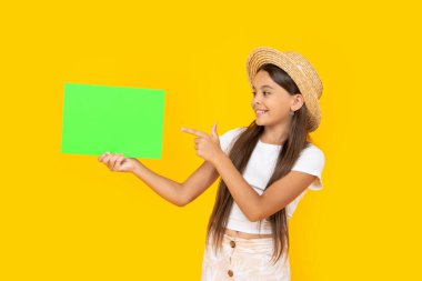 happy teen girl with copy space on green paper on yellow background. point finger.