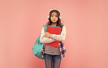 Üzgün çocuk dinle kulaklıkla müzik pembe arka planda çalışma kitabı olan sırt çantası taşır..
