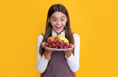 happy amazed child hold fresh fruit plate on yellow background. vitamins.
