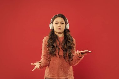 Kafası karışmış çocuk kazak giyiyor. Duygularını ifade et. Sonbahar modası. Kulaklık takan genç kız akıllı telefon kullanıyor. çocukluktaki modern hayat. Ses kitaplarını dinliyordum. çocuk kulaklıkla müzik dinle.