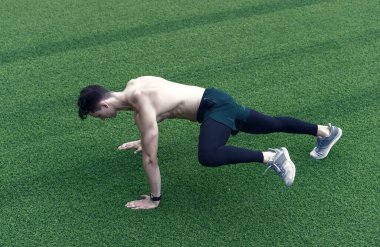 Atletik adam kalas egzersizi yapıyor. Yeşil çimlerde kas sporcusu eğitimi. Nefes alırken koş. Sporcu vücudunun alt ve üst kısımlarını çimenlerde sıkı bir şekilde çalıştırır. Temiz hava eğitimi..