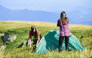 Helpful to have partner for raising tent. Attach necessary structural components tent. Prepare for night. Girl scout concept. Women set up tent on top mountain. Camping hiking. Hiking activity.