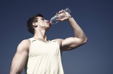 Vücut kas el kasları pazı, triceps ile. Spor ve fitness kavramı. Sağlıklı yaşam ve sağlık. Adam içme suyu şişe güneşli. Mavi gökyüzü üzerinde yeşil tshirt atlet.