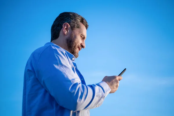 cheerful man chat on smartphone with message. man chatting on phone messaging. smartphone communication. man chat on sky background.