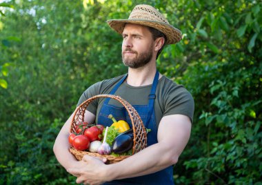 gardener in straw hat hold basket full of vegetables.