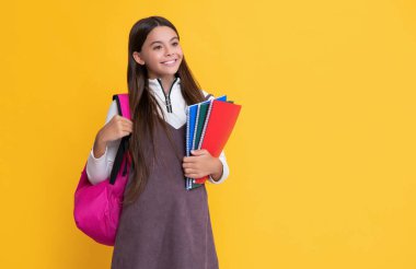 smiling child with school backpack and workbook on yellow background.