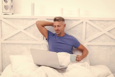 Yatakta dinlenmek. Mutlu adam laptopla kahve içer. Sabah rahatlaması. Çevrimiçi sohbet. İnternet videosunun keyfini çıkarıyorum.