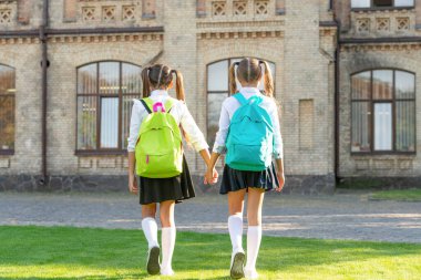 back view of two children with school backpack walking together outdoor.