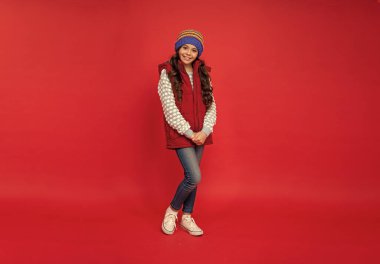 Kalın giysiler giyen bir çocuk. Olumlu duygularını ifade et. Kış modası. Şapkalı, kıvırcık saçlı, pozitif çocuk. Kadın manken. Yelek giyen genç kız..