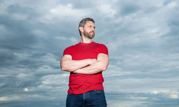 Confident guy sky background. Serious guy keeping arms crossed. Grizzled guy in casual outdoors.