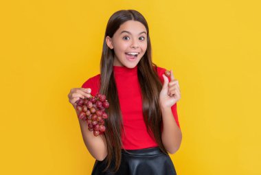 surprised teen child hold bunch of grapes on yellow background.