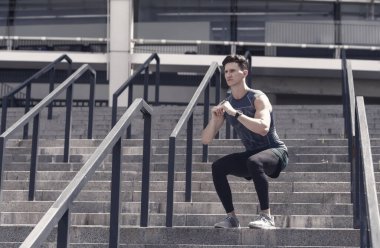 Egzersiz ve sağlıklı yaşam tarzı kavramı. Adam dışarıda çömeliyor. Adam spor yapıyor ve çömelme hareketleri yapıyor. Derin çömelmeler. Spor kıyafetli genç adam dışarıda çömeliyor..