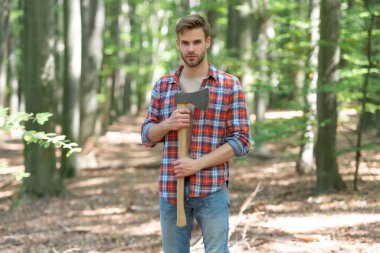 Unshaven guy in lumberjack style standing with axe forest background.