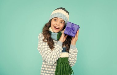 Örgü giysi kutusundaki meraklı mutlu çocuk. Hediyesi olan çocuk. Mavi arka planda genç bir kız. kış tatili.