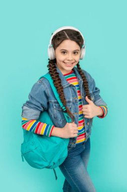 Happy girl giving thumb gesture. Teen girl listening to music blue background. Teenage girl back to school. Non-formal education.