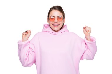 Happy girl smiling making winning gesture in casual pink hoodie and glasses isolated on white.